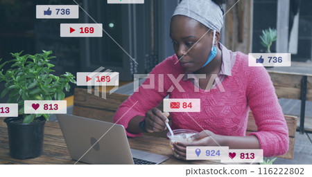 Image of social media icon over african american woman having a snack and using laptop at a cafe 116222802