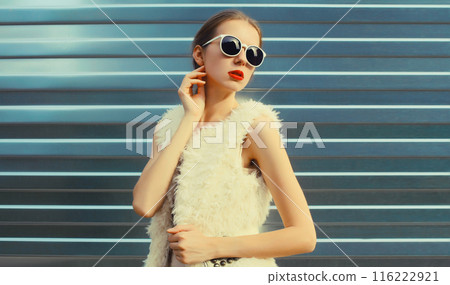 Modern stylish young woman in white fur vest, glasses, fashionable girl posing on gray background Modern stylish young woman in white fur vest, glasses, fashionable girl posing on gray background 116222921