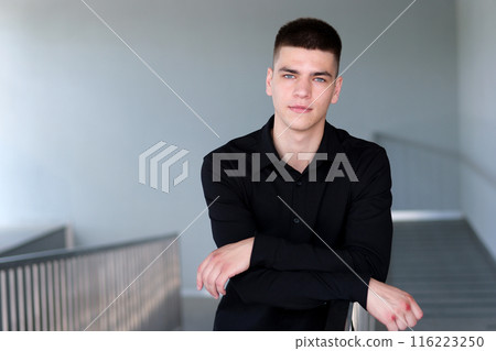 Guy in glass office. Handsome man with black hair and blue eyes. Caucasian businessman walking indoor in office company browsing scrolling phone mobile app looking outside pensive Guy in glass office. Handsome man with black hair and blue eyes. Caucasian businessman walking indoor in office company browsing scrolling phone mobile app looking outside pensive 116223250