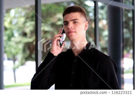 Subject businessman angry speaks on phone. Young caucasian brunette male in shirt. Small business worker. Profession. Sales manager. Realtor uses smartphone. Emotion anger and hatred against building. 116223321