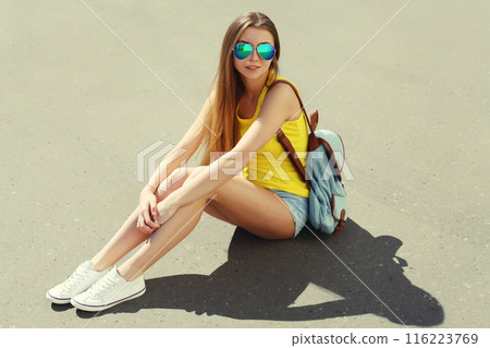 Stylish teenager girl with backpack, young woman sitting on city street on a summer day 116223769