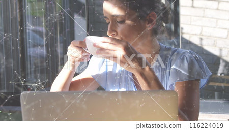 Young Caucasian woman drinking coffee while working on laptop Young Caucasian woman drinking coffee while working on laptop 116224019