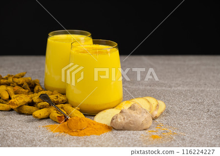 Golden milk, a traditional Ayurvedic drink with turmeric in two glasses on a black gray background 116224227