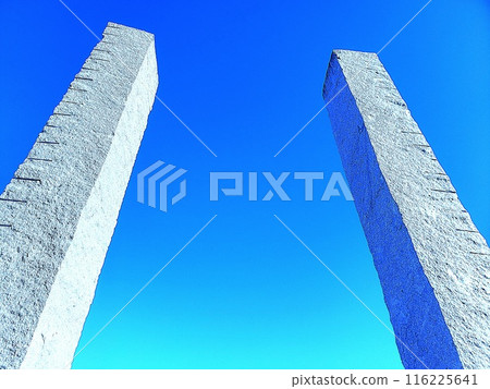 Two white stone pillars shining against the blue sky 116225641