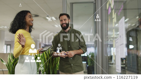 Image of profile icons floating over diverse man and woman discussing over memo notes at office Image of profile icons floating over diverse man and woman discussing over memo notes at office 116227119