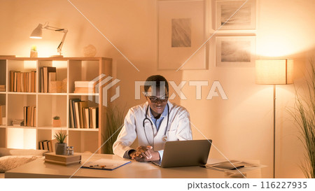 Telehealth consulting. Video call. Virtual doctor. Distance checkup. Male physician in white coat discussing therapy working online using laptop in modern interior with copy space. 116227935