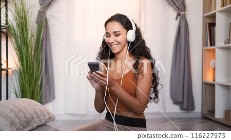 Music app. Phone playlist. Gadget entertainment. Relaxed smiling woman in headphones enjoying listening to song at light modern home interior with free space. Music app. Phone playlist. Gadget entertainment. Relaxed smiling woman in headphones enjoying listening to song at light modern home interior with free space. 116227975