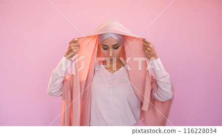 Hijab choice. Muslim female freedom. Unhappy sad woman covering head wearing headscarf traditional islamic clothing isolated on pink copy space background. Hijab choice. Muslim female freedom. Unhappy sad woman covering head wearing headscarf traditional islamic clothing isolated on pink copy space background. 116228034
