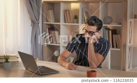 Distance education. Tired student. Online lecture. Weary man in video virtual class on laptop falling asleep at desk sitting in home living room. 116228035