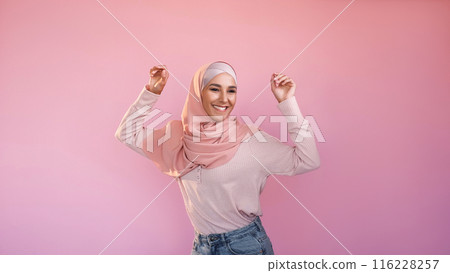 Happy dance. Good mood. Success celebration. Joyful optimistic carefree woman in hijab having fun isolated on pink empty space background. Happy dance. Good mood. Success celebration. Joyful optimistic carefree woman in hijab having fun isolated on pink empty space background. 116228257
