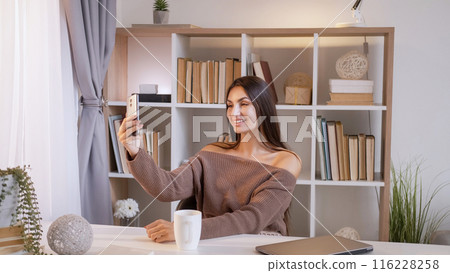 Online communication. Mobile connection. Happy joyful casual woman sitting at home desk talking smartphone gadget video call in living room. Online communication. Mobile connection. Happy joyful casual woman sitting at home desk talking smartphone gadget video call in living room. 116228258