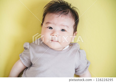Baby girl lying on a yellow background 116228295