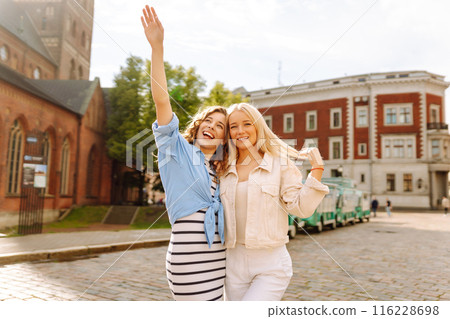 Smiling girlfriends are having fun on a sunny day on the streets of the city. Active lifestyle. 116228698