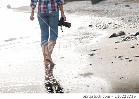Female photographer strolling on beach at sunrise Female photographer strolling on beach at sunrise 116228739