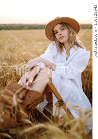 Young woman in white linen dress and hat enjoying a sunny day in a golden wheat field. Summer, beauty. Young woman in white linen dress and hat enjoying a sunny day in a golden wheat field. Summer, beauty. 116228942