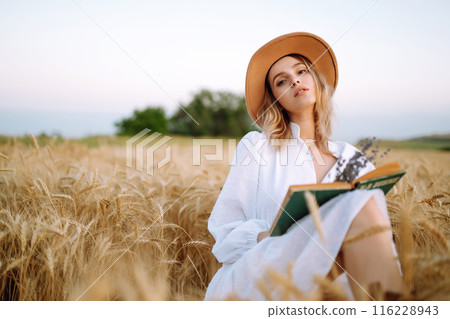 Young woman in white linen dress and hat enjoying a sunny day in a golden wheat field. Summer, beauty. 116228943