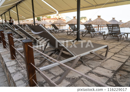 Beach sunbeds, chairs on beach on seaside resort, coastal town leisure area, relaxation, empty coastal chairs 116229017