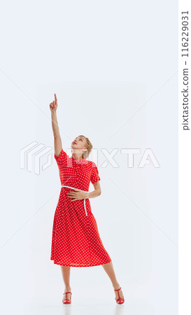 Full-length image of young beautiful woman in red dress pointing upwards, isolated on white background. Vertical image. Full-length image of young beautiful woman in red dress pointing upwards, isolated on white background. Vertical image. 116229031