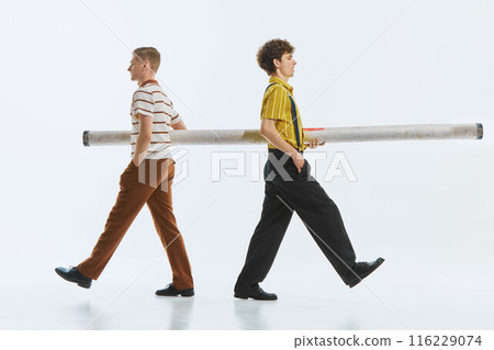 Two men in retro attire carry long tube isolated on white background. Teamwork and cooperation, working together to achieve common goals. Two men in retro attire carry long tube isolated on white background. Teamwork and cooperation, working together to achieve common goals. 116229074