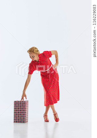 Dressed in a vibrant red polka dot dress, a woman poses with a wrapped gift isolated on white background. Holiday spirit. 116229083