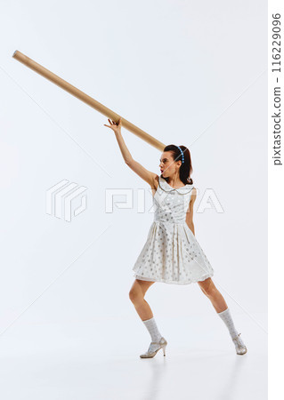 Dressed in a polka dot dress, a woman strikes a dynamic pose with a cardboard tube, showing motivated emotions. New start, beginning, startup launching Dressed in a polka dot dress, a woman strikes a dynamic pose with a cardboard tube, showing motivated emotions. New start, beginning, startup launching 116229096