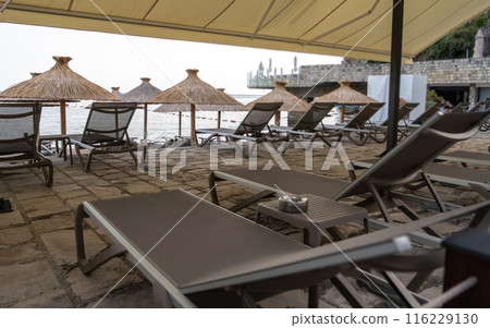 Beach sunbeds, chairs on beach on seaside resort, coastal town leisure area, relaxation, empty coastal chairs 116229130