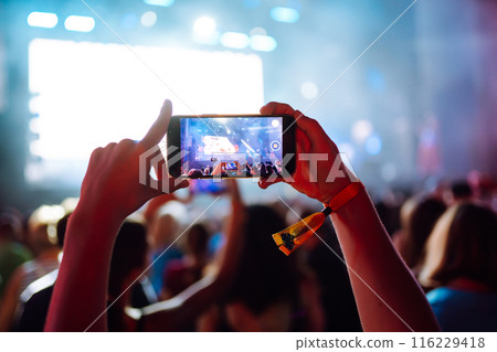 Hand with a phone records live music festival. People taking photographs with smart phone. 116229418
