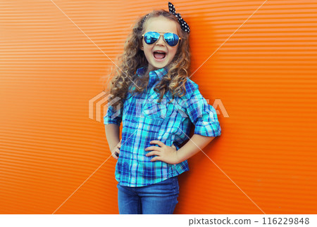 Happy cheerful kid girl with curly hair, joyful little child having fun in the city on orange wall 116229848