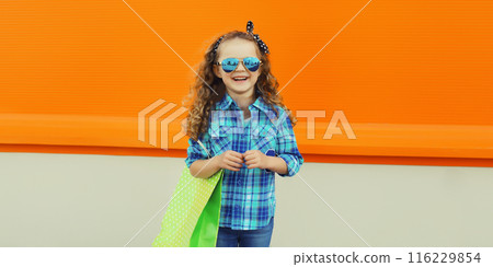 Stylish happy joyful kid girl standing with shopping bag, cheerful little girl child on city street Stylish happy joyful kid girl standing with shopping bag, cheerful little girl child on city street 116229854