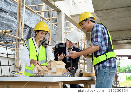 Engineers and businessman examining blueprints at table with architectural models in the foreground 116230564
