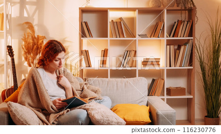 Book lifestyle. Home reading. Relaxed calm woman wrapped warm blanket on couch enjoying rest weekend leisure interesting story at cozy living room interior with free space. 116230776