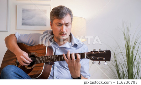 Music practicing. String performance. Creative hobby. Casual emotional talented man artist playing acoustic guitar melody enjoying leisure at home. 116230795