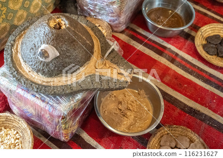 Traditional argan oil production setup, stone grinder, argan seeds, woven baskets, metal bowls, brown paste Traditional argan oil production setup, stone grinder, argan seeds, woven baskets, metal bowls, brown paste 116231627