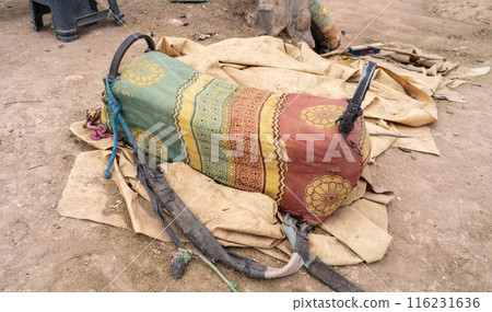 Camel saddle used for tourist rides in Morocco. Old fabric covering the saddle, worn straps, dusty ground 116231636