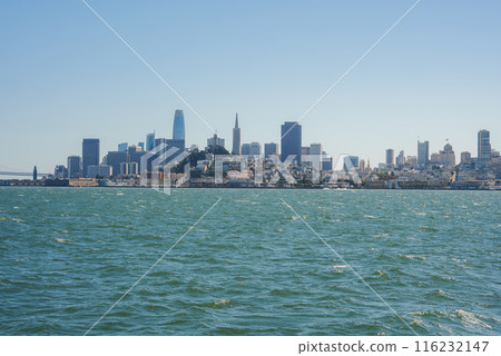 Panoramic view of San Francisco skyline from across the bay with city buildings creating a silhouette against a clear blue sky. No fog, iconic bridge, or boats in sight. Panoramic view of San Francisco skyline from across the bay with city buildings creating a silhouette against a clear blue sky. No fog, iconic bridge, or boats in sight. 116232147