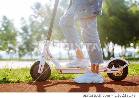 Young female legs on electric scooter. Woman rides electric scooter in park. Active lifestyle. 116232172