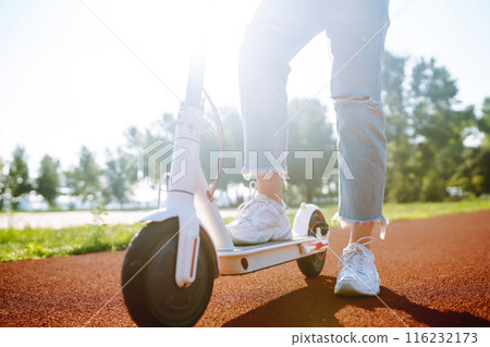 Young female legs on electric scooter. Woman rides electric scooter in park. Active lifestyle. Young female legs on electric scooter. Woman rides electric scooter in park. Active lifestyle. 116232173