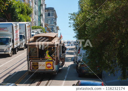 Classic San Francisco cable car ascending steep street with Victorian architecture and lush green trees. Blend of tourism and daily life. Sunny day vibe. Classic San Francisco cable car ascending steep street with Victorian architecture and lush green trees. Blend of tourism and daily life. Sunny day vibe. 116232174