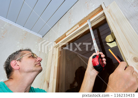 Measuring sauna doors doorway before lining jamb, carpenter uses tape measure and pencil to mark. 116233433