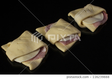 Semi-finished puff pastry with sausage and cheese on a black background Semi-finished puff pastry with sausage and cheese on a black background 116239888