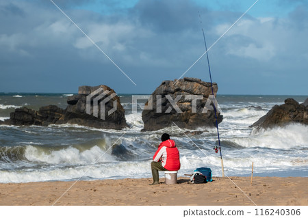 Fisherman on the sandy beach of the Atlantic Ocean in winter, man alone by the sea, beautiful cloudscape, dramatic landscape, gloomy seascape, big sea waves 116240306
