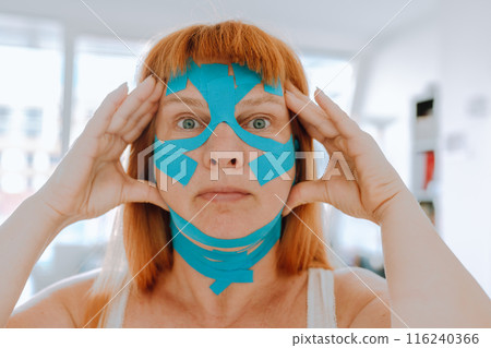 Close-up portrait middle-aged woman, she puts kinesiology tape on face 116240366