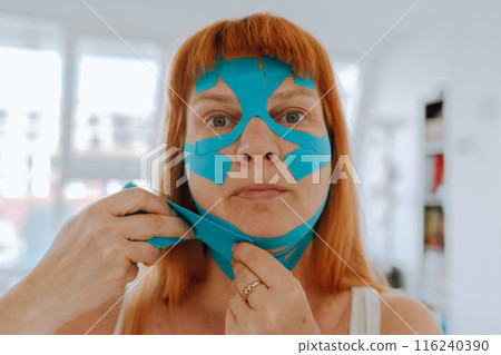Close-up portrait middle-aged woman, she puts kinesiology tape on face Close-up portrait middle-aged woman, she puts kinesiology tape on face 116240390