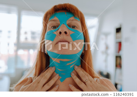 Close-up portrait middle-aged woman, she puts kinesiology tape on face Close-up portrait middle-aged woman, she puts kinesiology tape on face 116240391