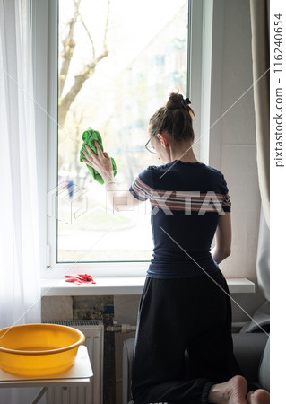 Young woman washes a window on the first floor with a rag in her hand, close-up. Cleaning windows at home 116240654