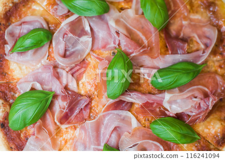 Delicious pizza slices with prosciutto, cheese and basil. Close-up of a pizza in the American style. Delicious pizza slices with prosciutto, cheese and basil. Close-up of a pizza in the American style. 116241094
