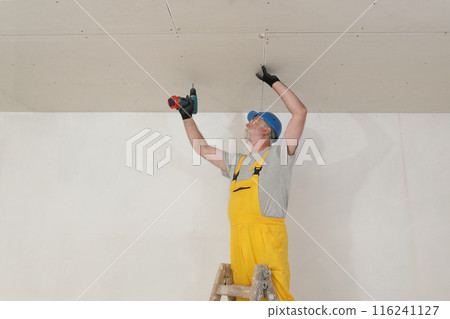 Senior adult worker fixing gypsum ceiling using screwdriver 116241127