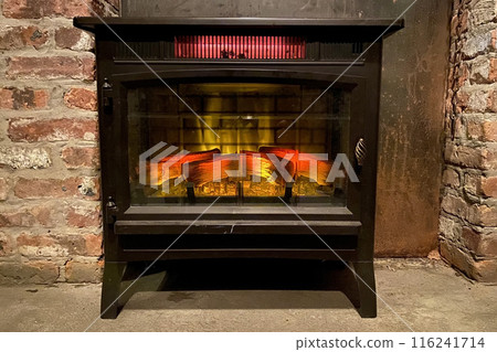 Fireplace with burning firewood in the interior of a restaurant. A cozy scene with a crackling fireplace set against a rustic brick wall, radiating warmth and comfort. Fireplace with burning firewood in the interior of a restaurant. A cozy scene with a crackling fireplace set against a rustic brick wall, radiating warmth and comfort. 116241714