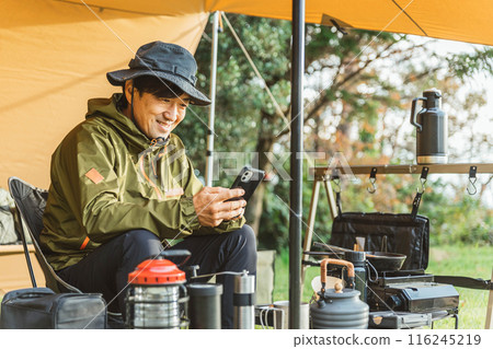 A middle-aged male camper looking at his smartphone while solo camping 116245219