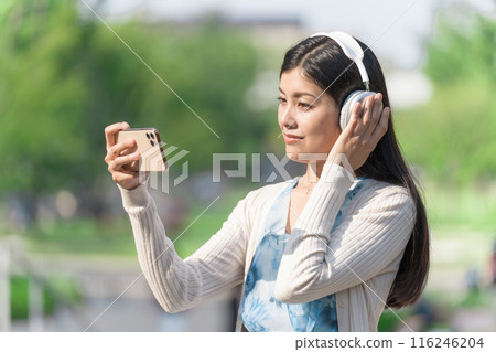 A young woman wearing headphones and watching videos on her smartphone 116246204